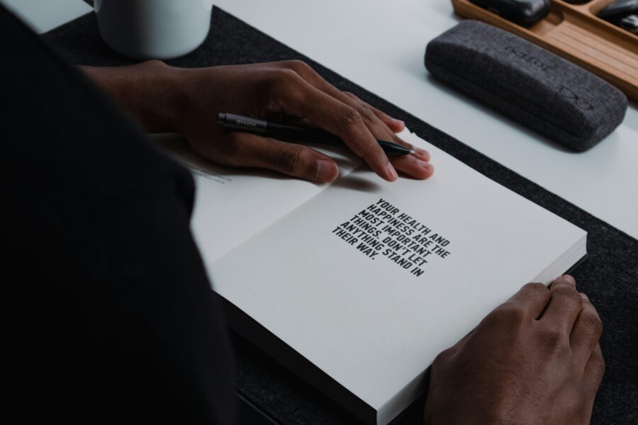Person journaling for mental health, writing in a journal with the printed quote “Your health and happiness are the most important things. Don’t let anything stand in their way.”